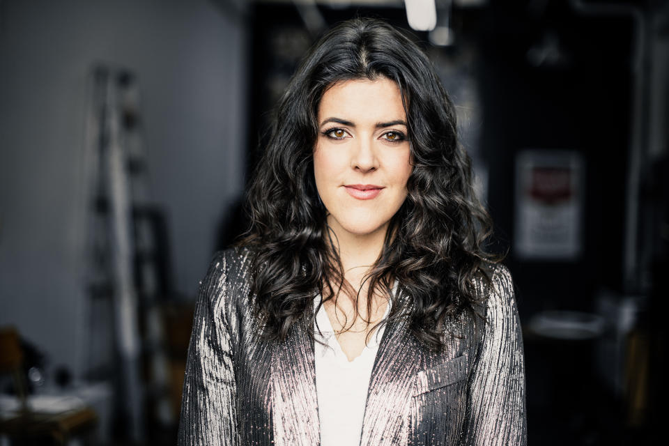 a woman in a silver jacket stands in a dark room