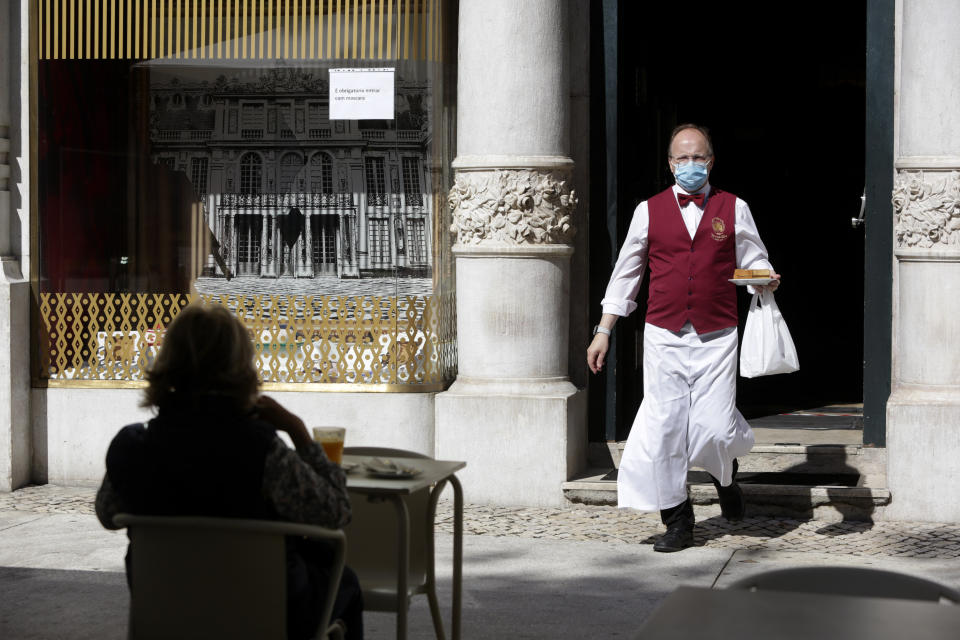 FILE - In this Monday, May 18, 2020 file photo, a waiter, wearing a protective face mask, brings an order to a customer sitting outdoors at the Versailles restaurant and pastry shop in Lisbon, Portugal. The coronavirus pandemic is gathering strength again in Europe and, with winter coming, its restaurant industry is struggling. The spring lockdowns were already devastating for many, and now a new set restrictions is dealing a second blow. Some governments have ordered restaurants closed; others have imposed restrictions curtailing how they operate. (AP Photo/Armando Franca, File)