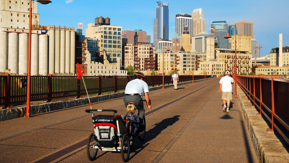 Minneapolis, MN, USA May 14, 2013 An adult man commutes to work, carrying his child in a bicycle trailer, crossing the Stone Arch Bridge in Minneapolis, Minnesota - Image.