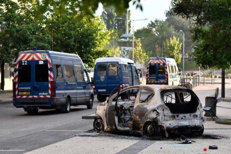 Des véhicules de police passent à proximité d'une voiture incendiée dans le quartier des Grésilles, le 15 juin 2020 à Dijon - Philippe DESMAZES © 2019 AFP