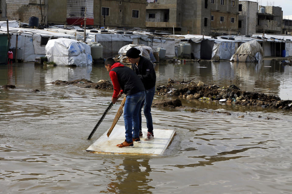 Refugiados sirios utilizan un pedazo de madera flotante para trasladarse después de que fuertes lluvias inundaran un campo de refugiados en el pueblo de Bar Elias en el valle Bekaa, Líbano, el jueves 10 de enero de 2019. (AP Foto/Bilal Hussein)