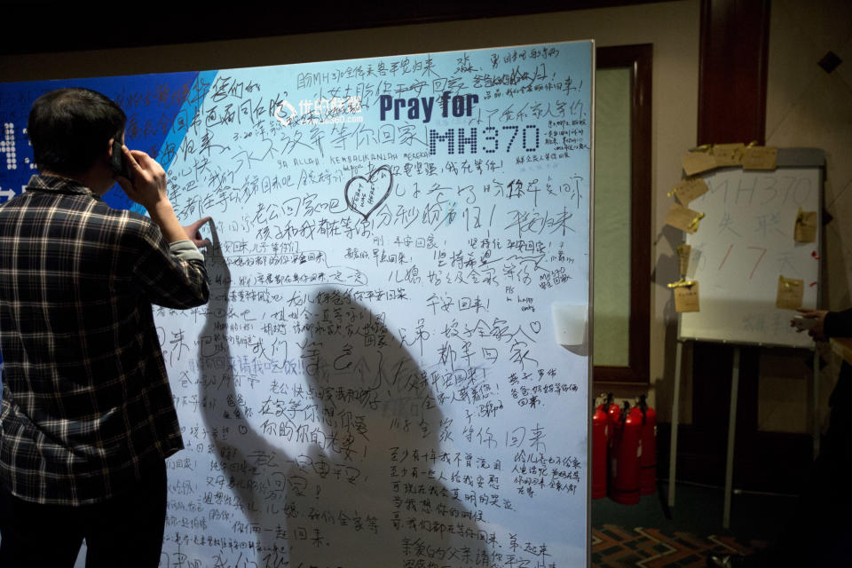 A man, one of the relatives of Chinese passengers onboard Malaysia Airlines Flight 370, talks on his mobile phone as he touches a board covered with written wishes, while a board, right, marks the 17th day since the flight lost contact, at a hotel in Beijing, China, Saturday, March 29, 2014. Some of the wishes are "Dear husband, you must stay strong, I am waiting for you. Dear father, please be back home safely and the whole family is here waiting for you." (AP Photo/Alexander F. Yuan)