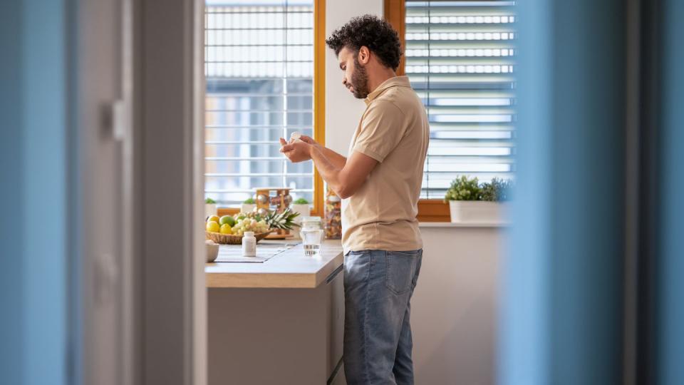 young man taking medicine with water at home