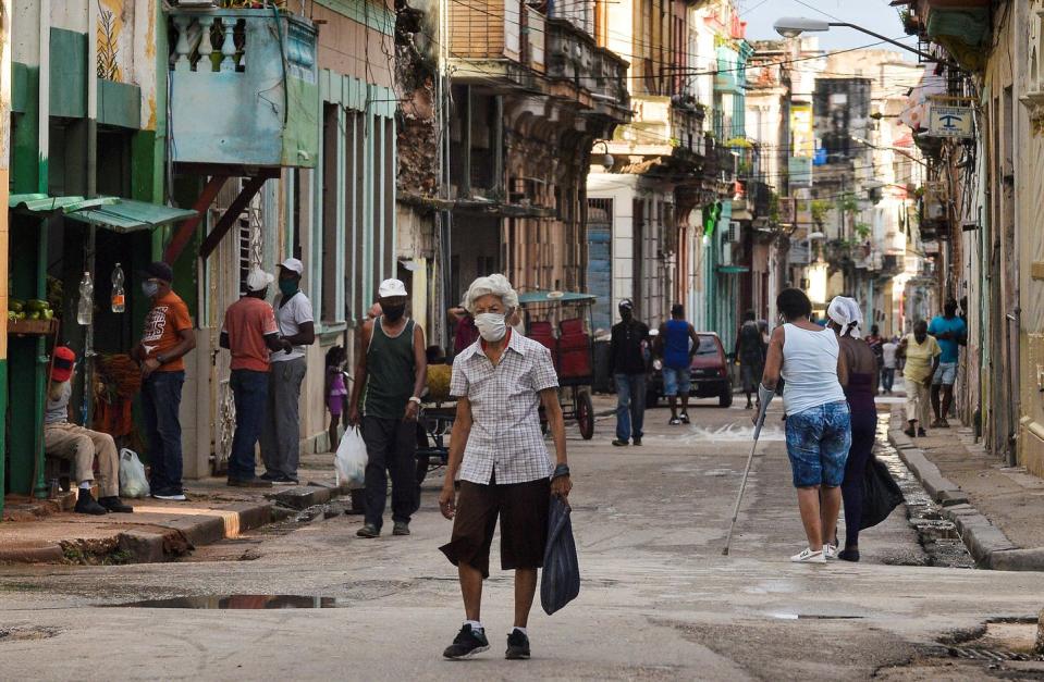 An elderly person wearing a face mask walks along a street of Havana, holding a grocery bag