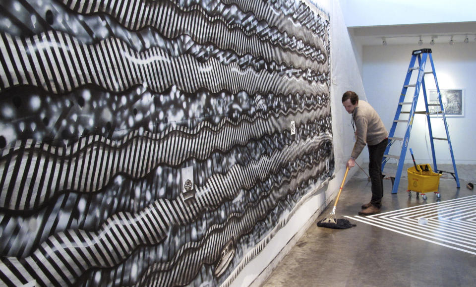 In this Tuesday, Feb. 19, 2013 photo, Ryan Travis Christian mops the floor in front of his wall-sized charcoal drawing at the Contemporary Art Museum in Raleigh, N.C. The Chicago artist completely reworked his drawing several days into his first museum exhibition. (AP Photo/Allen Breed)