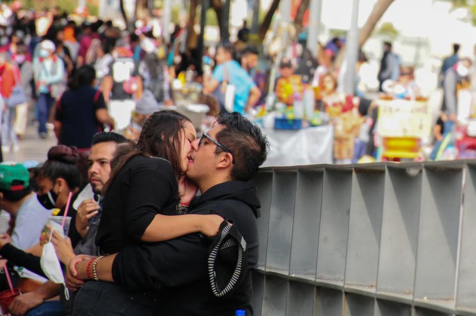Una pareja se besa en la explanada de Bellas Artes, en el fondo, decenas de personas caminan entre los comerciantes y sus puestos.