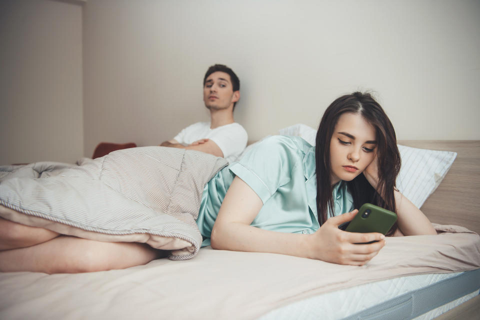 Jealous man watches over his girlfriend's shoulder as she texts in bed