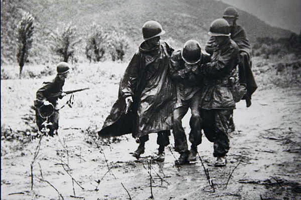 Capt. Emil Kapaun (right), former chaplain with Headquarters Company, 8th Cavalry Regiment, 1st Cavalry Division, helps another soldier carry an exhausted Soldier off the battlefield early in the Korean War.