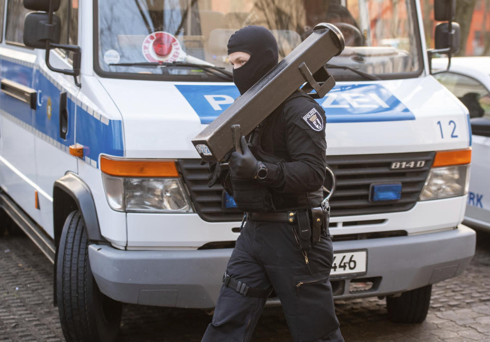 A police walks in front of a car during raids against an Islamist network at the Maerkische Viertel neighborhood in Berlin, Thursday, Feb. 25, 2021. Police searched the apartments of several alleged supporters of a banned Islamic extremist organization in the German capital. (Christophe Gateau/dpa via AP)