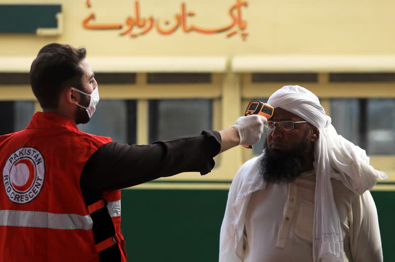 A worker checks a man's temperature following an outbreak of the coronavirus disease (COVID-19), at a railway station in Peshawar