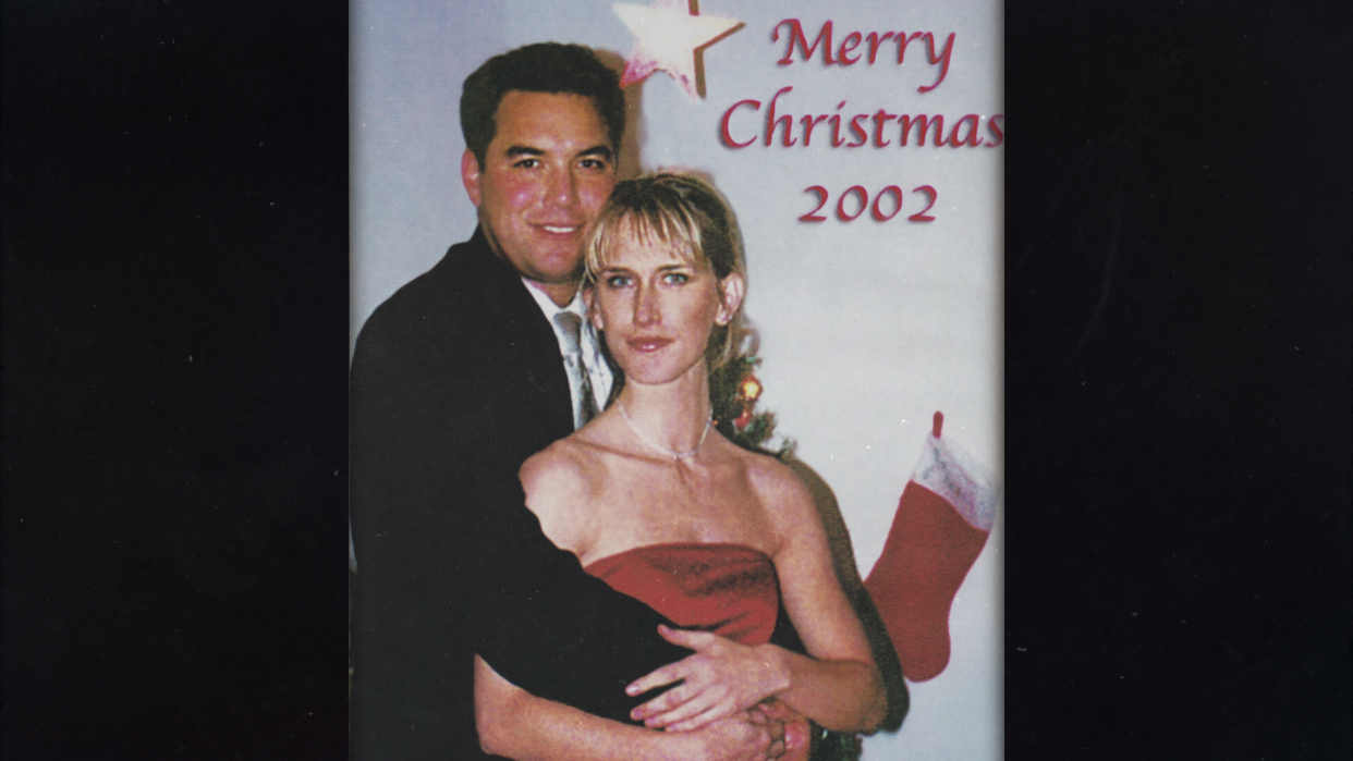 Scott Peterson and Amber Frey embrace in front of a backdrop reading: Merry Christmas 2002.