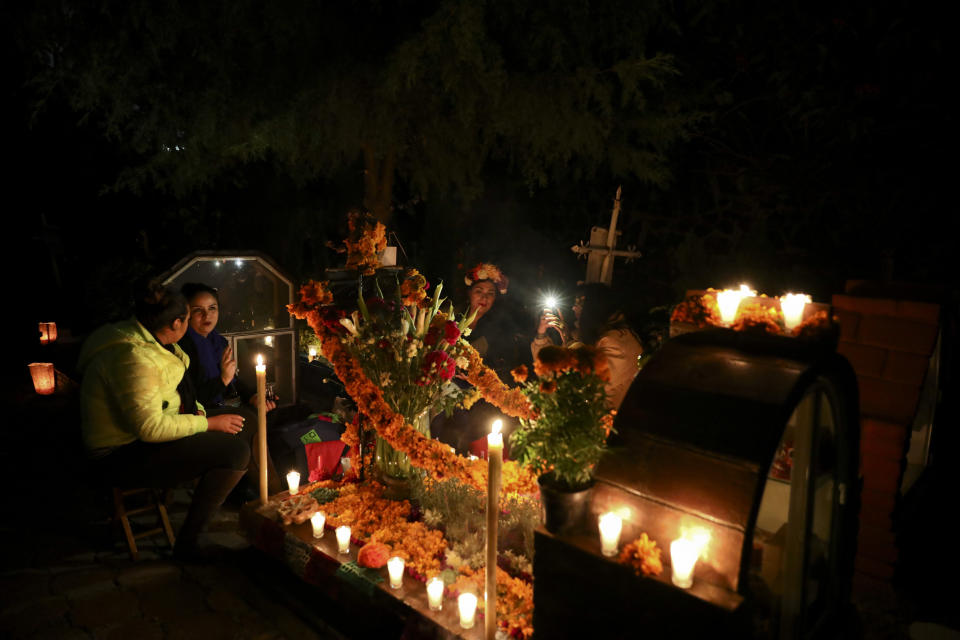 Relatives spend the night next to the tomb of their loved one in the Los Reyes cemetery during Day of the Dead festivities in Mexico City, Friday, Nov. 1, 2019. In a tradition that coincides with All Saints Day and All Souls Day, families decorate the graves of departed relatives with flowers and candles, and spend the night in the cemetery, eating and drinking as they keep company with their deceased loved ones. (AP Photo/Eduardo Verdugo)