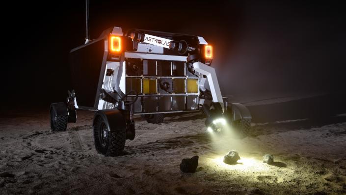 a wheeled lunar rover shines its headlights on a rock in the California desert