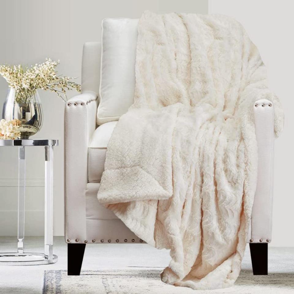 Warm, white, velvety throw blanket tossed over a white chair with nailhead trim.