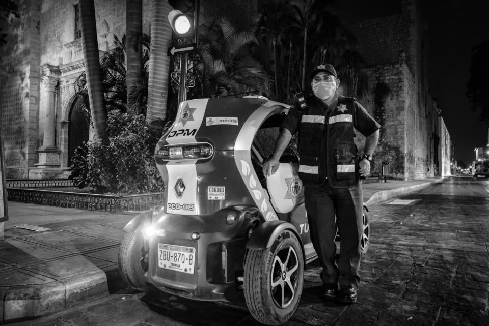 Un oficial de la Policí­a Turística de Mérida, equipado con cubreboca, hace guardia nocturna en un trecho de la calle 59, una ví­a muy utilizada que atraviesa todo el centro histórico y que ha sido sometida a un plan de cierres parciales temporales para limitar el flujo vehicular no esencial en esta parte de la ciudad durante la pandemia.