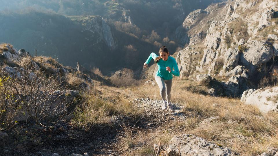 Beautiful, young female athlete running uphill.