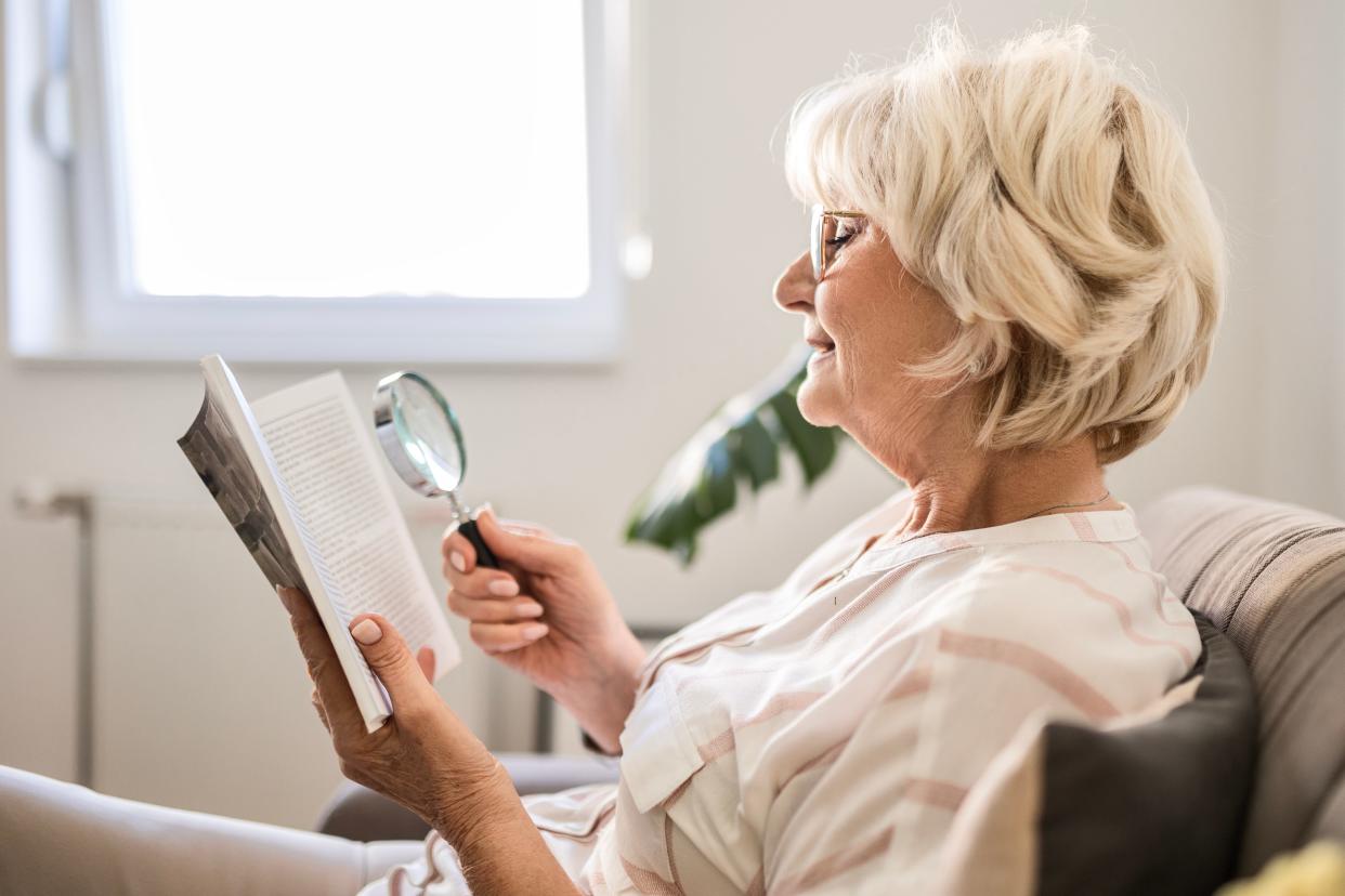 A woman reading a book using a magnifying glass