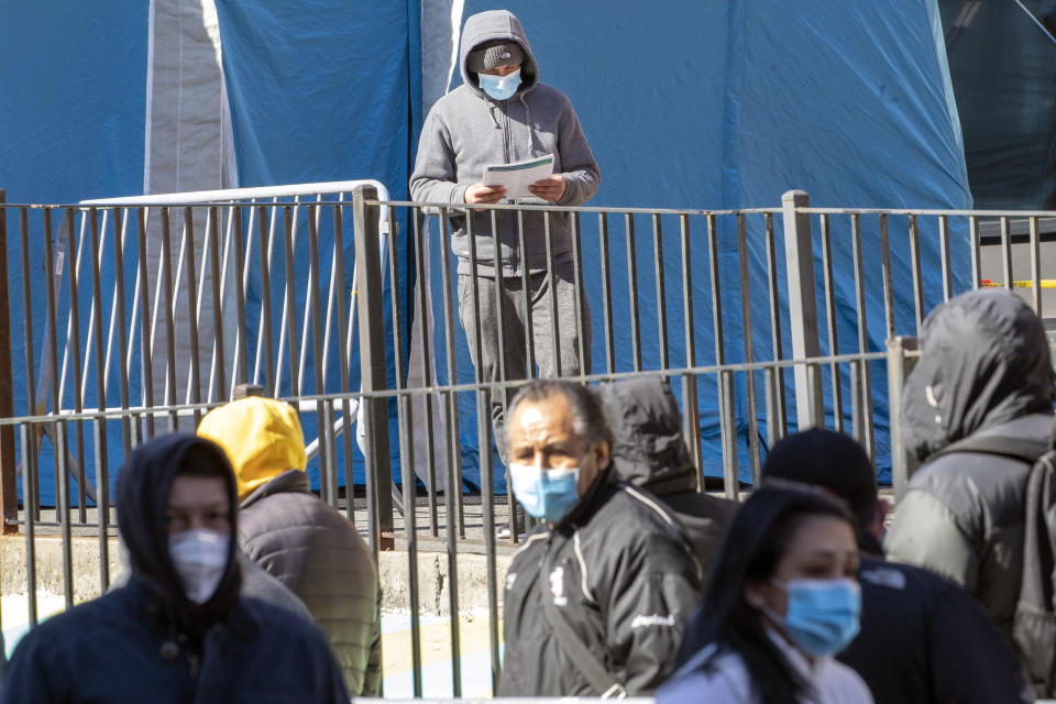 A man looks at over paperwork he was given after being tested for the coronavirus as the leaves the testing tent while others wait in line to be tested outside Elmhurst Hospital Center, Tuesday, March 24, 2020, in the Queens borough of New York. New York Gov. Andrew Cuomo says the number of positive coronavirus cases in the state surged to more than 20,000, with more than half the cases in New York City. Cuomo promised 1,000 temporary hospital beds will be swiftly placed inside a vast Manhattan convention center as officials raced to prepare for an overwhelming number of coronavirus patients. (AP Photo/Mary Altaffer)