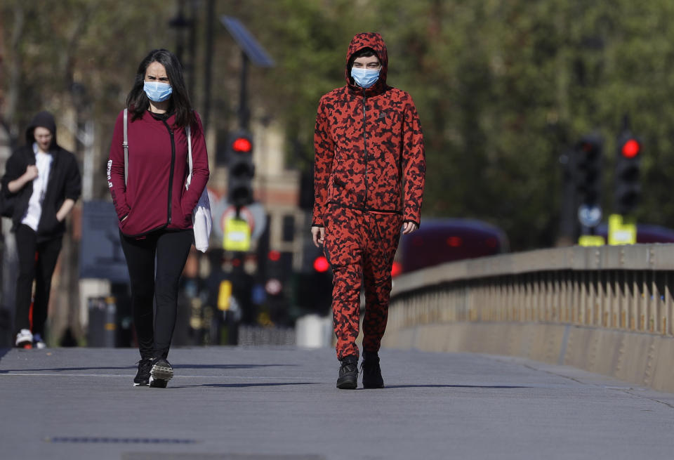 People wear protective face masks as they walk in Westminster in London, as the country is in lockdown to help curb the spread of coronavirus, Tuesday, April 21, 2020. (AP Photo/Kirsty Wigglesworth)