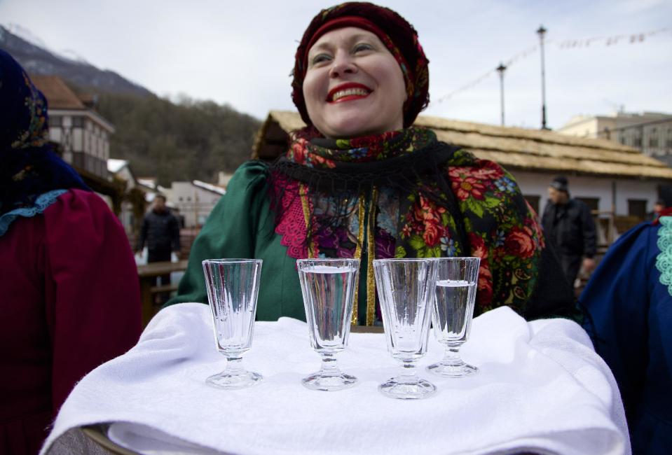 FILE - In this Feb. 6, 2013, file photo, a woman in a traditional folk costume welcomes guests with a beverage at a street in Rosa Khutor, some 60 km east of the Black Sea resort of Sochi, Russia. Sochi has long been a choice destination for Russia's political elite. Joseph Stalin's summer residence in Zeleni Mys even features a wax mannequin of the dictator at his desk. (AP Photo/Ivan Sekretarev, file)