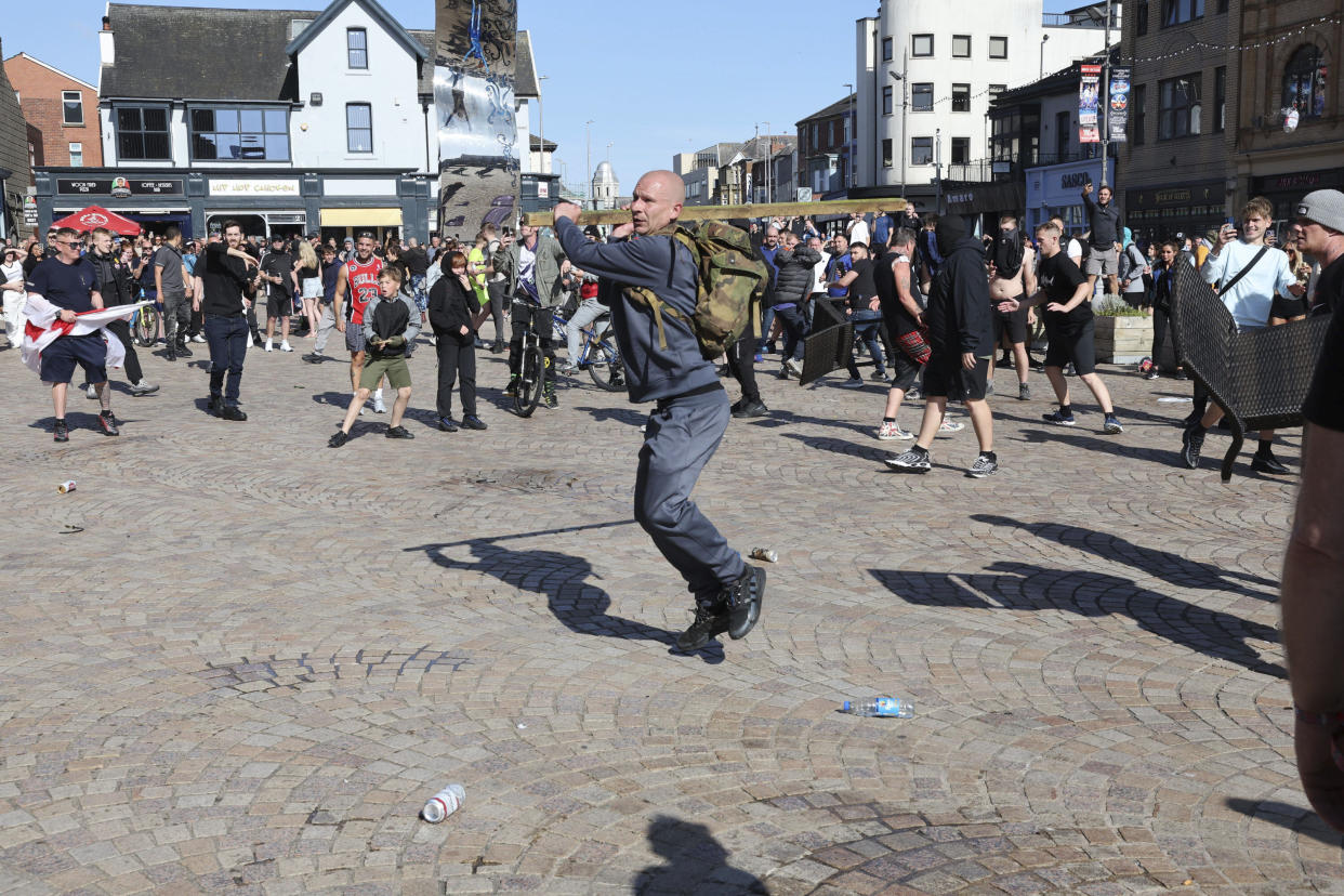 A man swings a length of wood as people protest in Blackpool, England