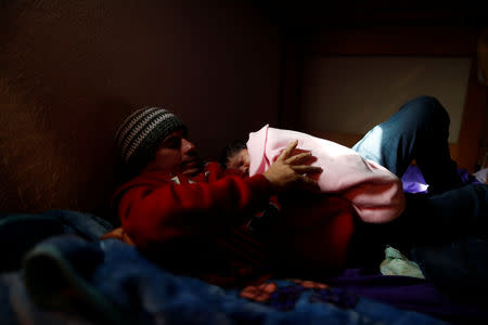 Honduran migrant Alvin Reyes, 39, holds his newborn son Alvin, as they lie on their bed in the dormitory of a church in Tijuana, Mexico, December 4, 2018. REUTERS/Carlos Garcia Rawlins