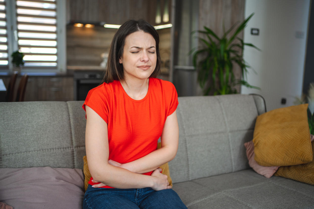 Frau mit Bauchschmerzen sietzt auf dem Sofa