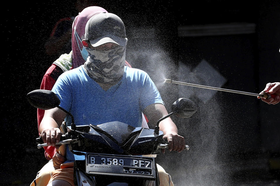 Motorists are sprayed with disinfectant in an attempt to curb the spread of coronavirus outbreak at the gate of a housing complex in South Tangerang, Indonesia, Tuesday, March 31, 2020. Indonesia will close its doors to foreign arrivals in an attempt to curb the coronavirus spread while the country plans to bring home more than a million nationals working abroad. (AP Photo/Tatan Syuflana)