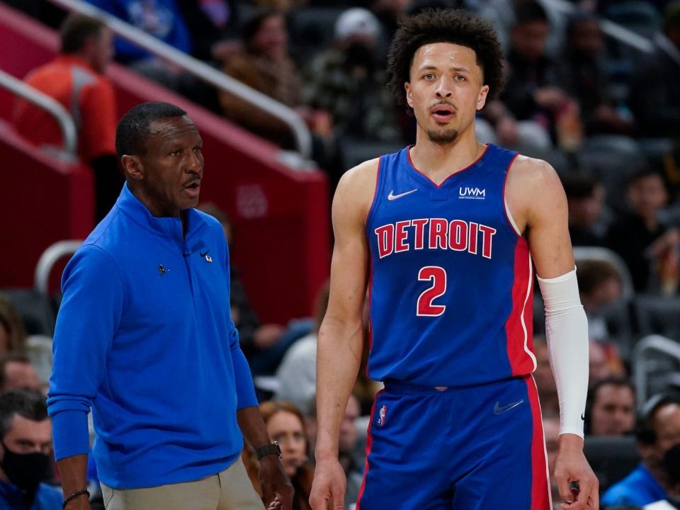 Cade Cunningham looks on while standing next to Dwane Case near the sidelines during a Pistons game.