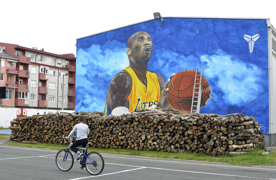 A boy rides a bicycle in front of a new tribute mural honoring former Los Angeles Lakers star Kobe Bryant who was killed in a helicopter crash on Jan. 26, on the school building in Bosanska Gradiska, Bosnia, Wednesday, June 3, 2020. (AP Photo/Radivoje Pavicic)