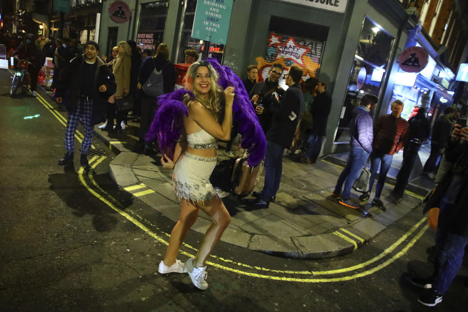A woman dances with purple feathers in the West End of London after pubs close, before London moves into the highest tier of coronavirus restrictions from Wednesday as a result of soaring case rates, Tuesday Dec. 15, 2020. (Aaron Chown/PA via AP)