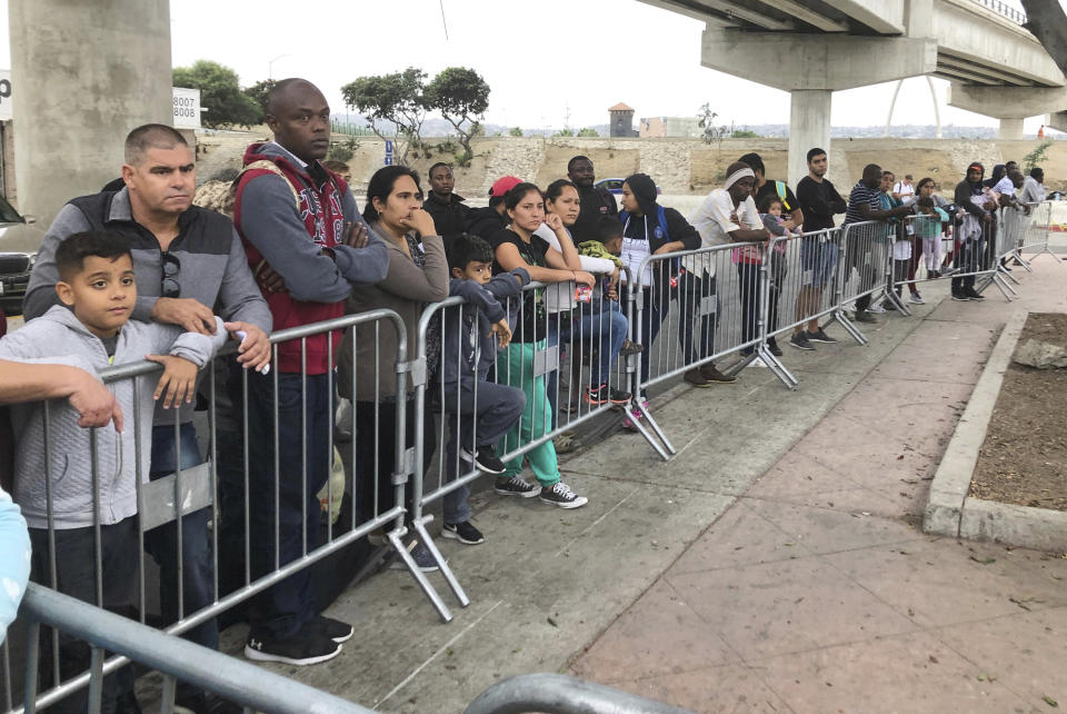 Asylum seekers in Tijuana, Mexico, listen to names being called from a waiting list to claim asylum at a border crossing in San Diego Thursday, Sept. 26, 2019. The Trump administration played "bait and switch" by instructing migrants to wait in Mexico for an opportunity to apply for asylum before imposing sharp restrictions on eligibility, attorneys said in a court filing Thursday. (AP Photo/Elliot Spagat)