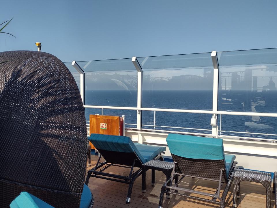 Two deck chairs on a cruise ship overlooking the water with a plant and sunshade behind them.