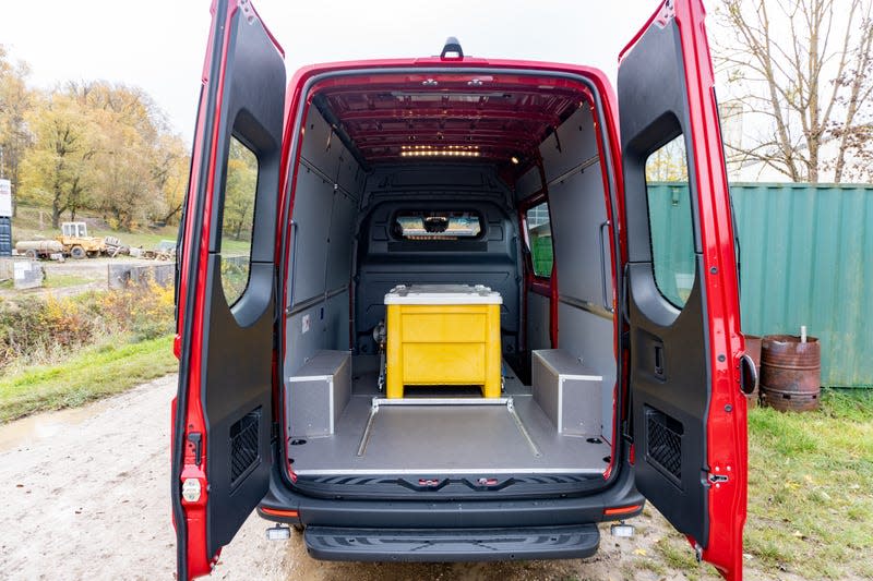 a view of the rear cargo area in a 2023 mercedes benz sprinter awd cargo van. the van is red, with both rear cargo doors open. a large yellow bin sits inside the van.