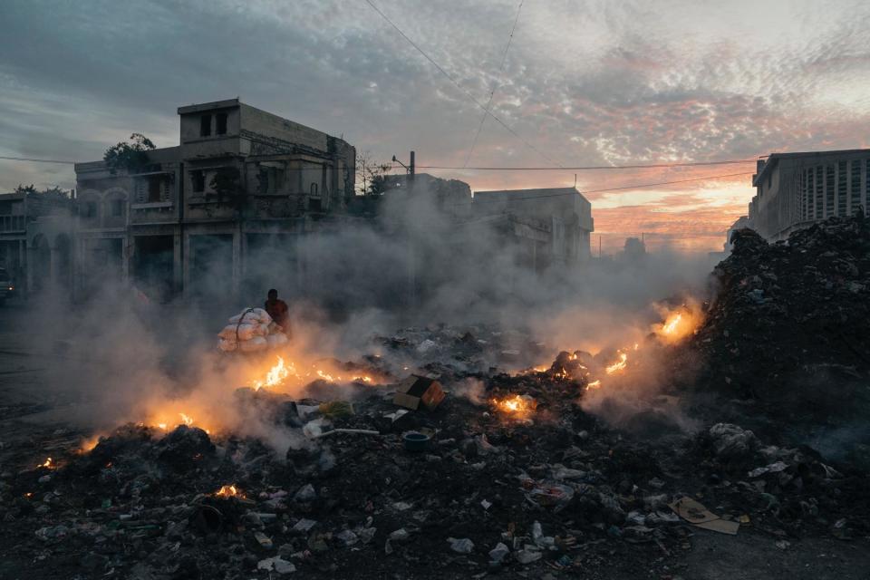 <br>A porter passes a burning trash pile on Boulevard Dessalines, Port-au- Prince.
