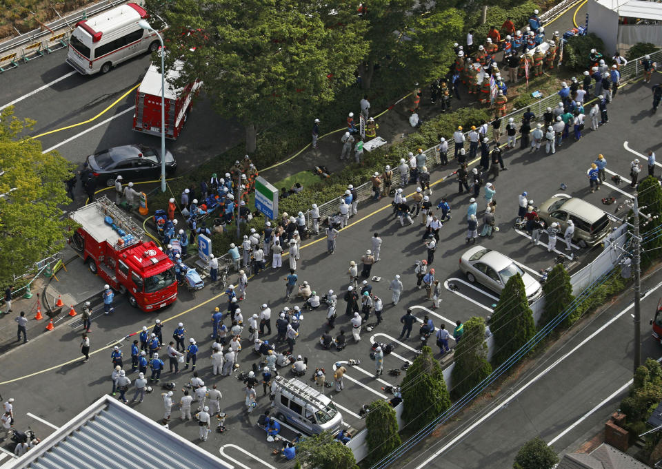 Rescue workers and workers believed to flee from the site of a fire gather outside a building under construction in Tama city, Tokyo's western suburbs Thursday, July 26, 2018. The fire broke out Thursday afternoon at the three-story building being constructed, injuring a number of people. (Kyodo News via AP)