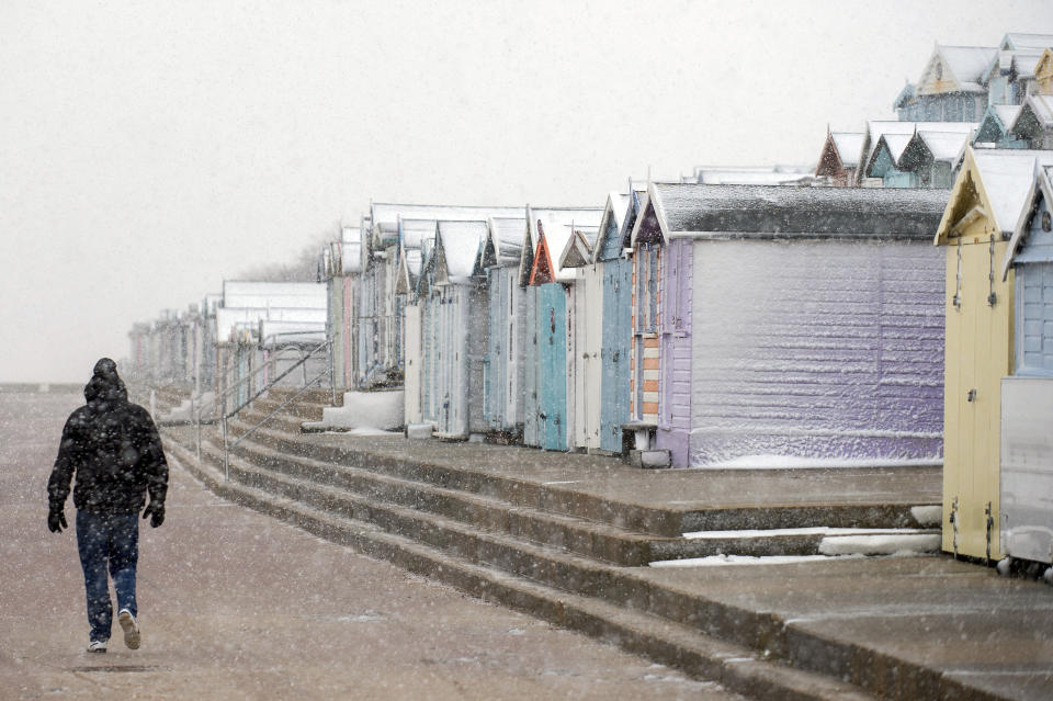 A person walks past snow covered beach huts at Walton-on-the-Naze, England, Sunday Feb. 7, 2021, with bitterly cold winds and heavy snow set to bring disruption to some parts of England. (Joe Giddens/PA via AP)