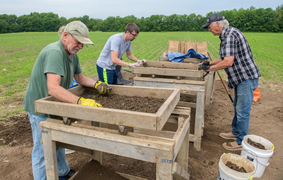 Volunteers Lynn Carl left, Steven Miller, middle, and Kerwin Brown sift through piles of dirt for artifacts like pieces of bone and pottery dug up from the site of an ancient Native American settlement recently discovered in a farm field in East Peoria.