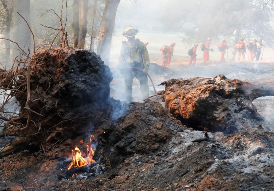 A firefighter hoses down a hot spot from the Fawn Fire as an inmate crew in the background hikes to a mop-up assignment off Old Oregon Trail on Friday, Sept. 24, 2021.