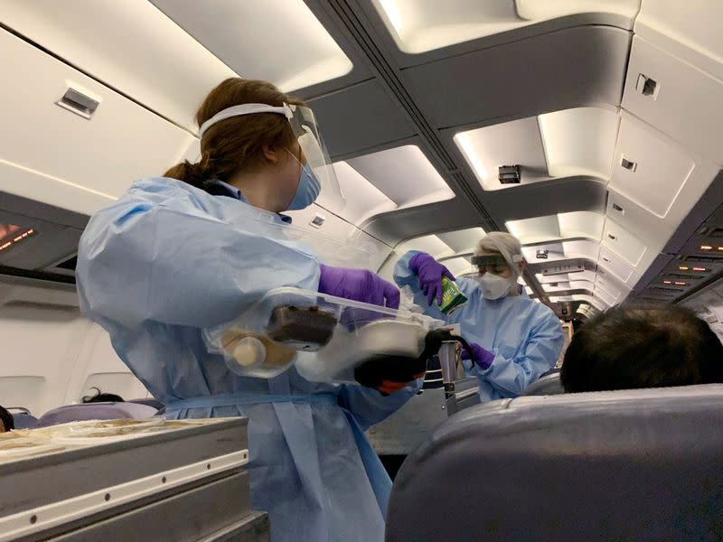 Flight attendants wearing protective clothing and masks serve snacks to evacuated Canadians