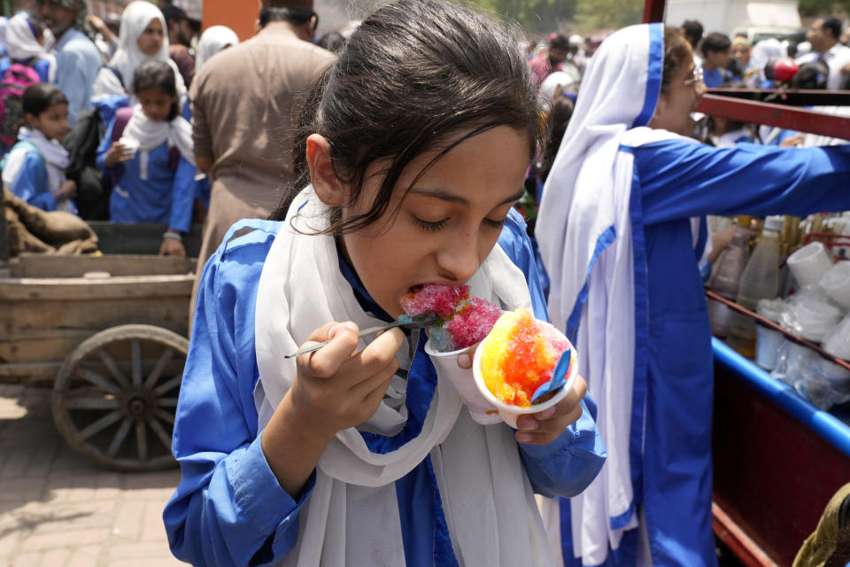 A student eats shaved ice as she leaves after school as authorities announced reduced school hours due to soaring temperature, in Lahore, Pakistan, Tuesday, May 21, 2024. Authorities in Pakistan on Tuesday urged people to stay indoors as the country is hit by an extreme heat wave that threatens to bring dangerously high temperatures and yet another round of glacial-driven floods. (AP Photo/K.M. Chaudary)