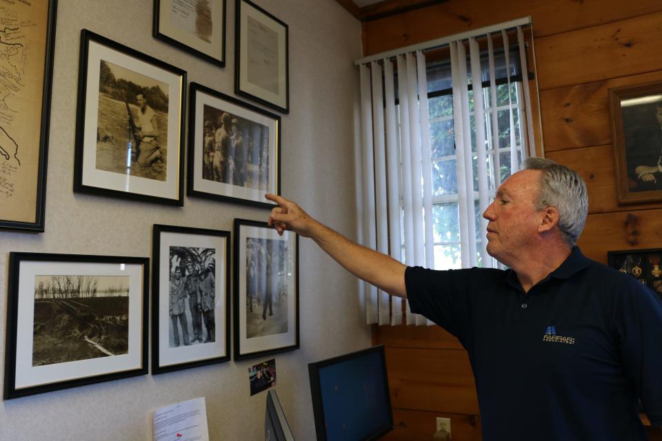 Jim Farrar points to photos of his father, William Farrar, during World War II that hang in his Bridge Street office.