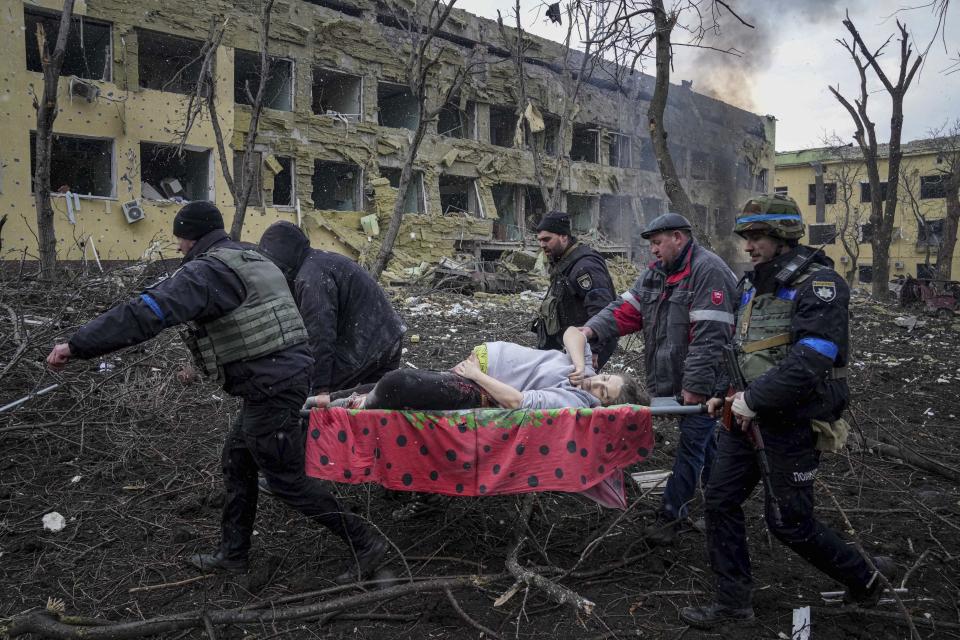 People carry an injured pregnant woman away from the damaged hospital on a stretcher.