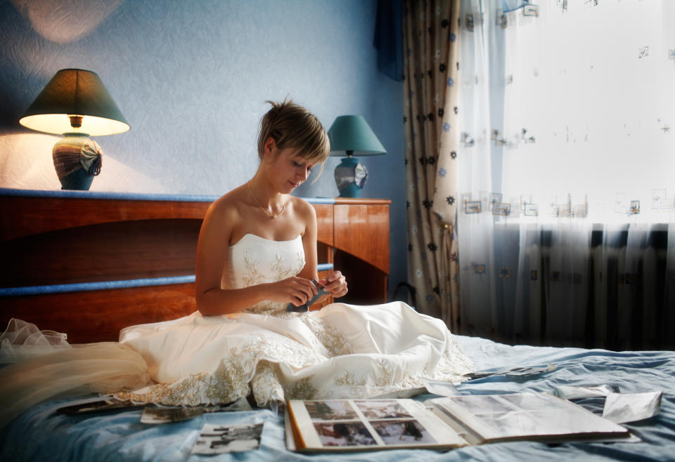 A bride sits on a bed looking at pictures