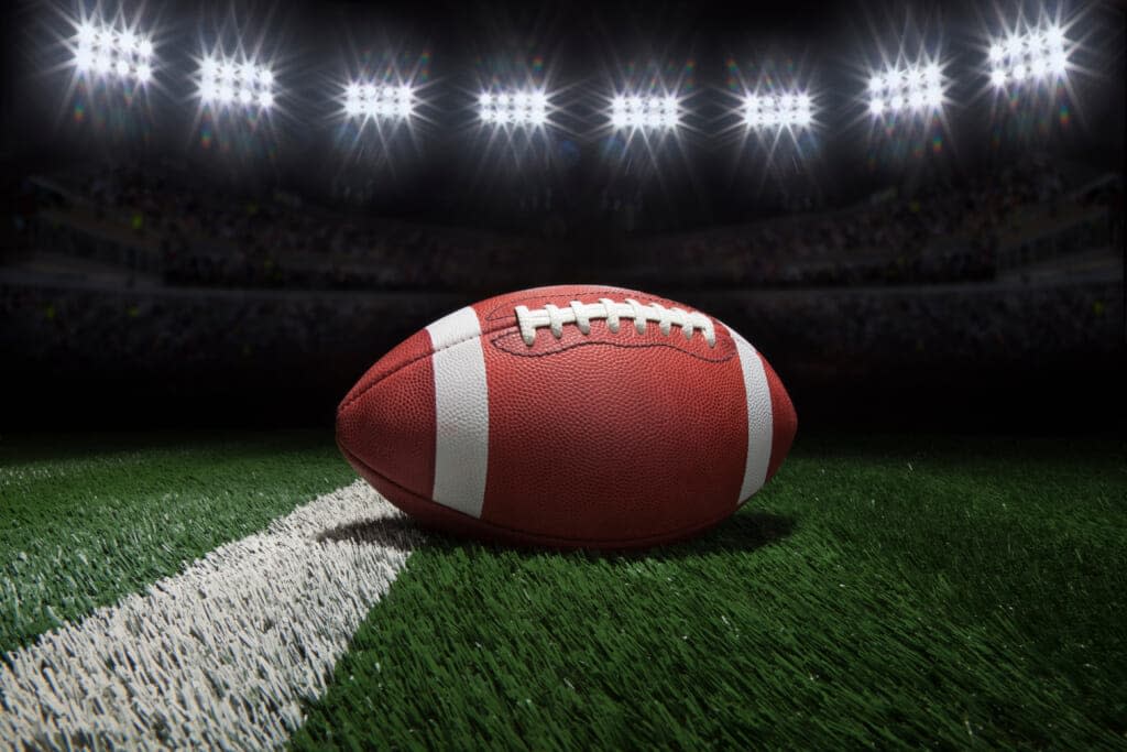 College style football on a yard line of a football field under stadium lights. (Adobe Stock)