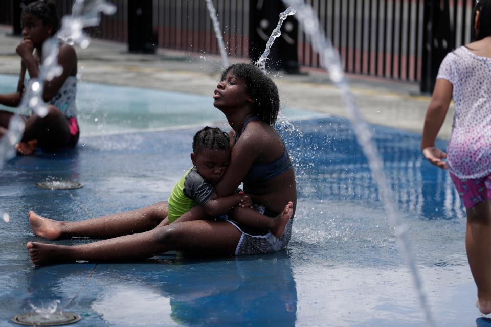 With her little cousin Jayden Thomas, 3, napping in her arms, Za-Kenya Byfield, 12, enjoys the water splashing against her head at the Cascades Park splash pad Sunday, June 23, 2019.