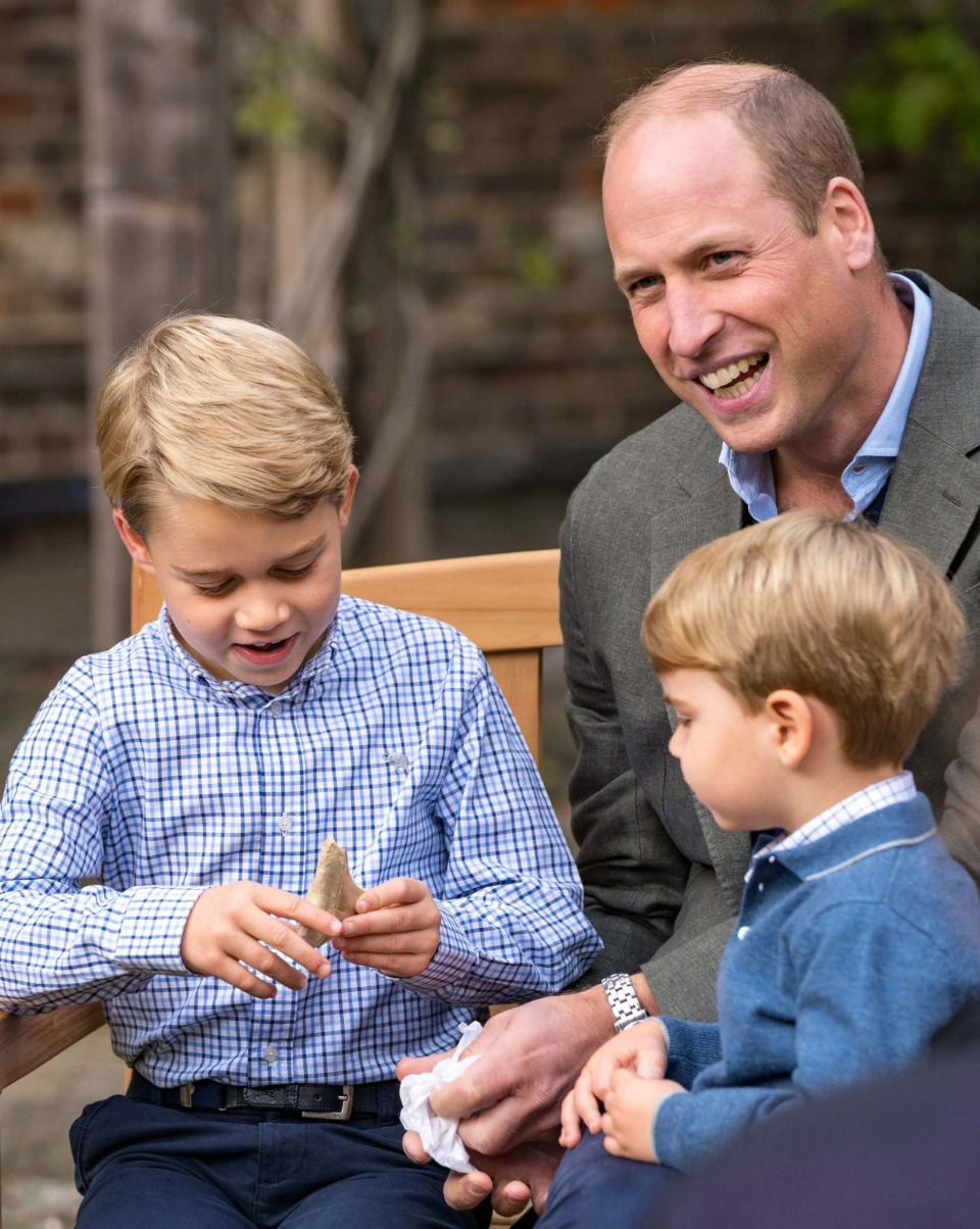 The Duke of Cambridge and Prince Louis watch as Prince George holds the tooth of a giant shark given to him by Sir David Attenborough in the gardens of Kensington Palace (PA)