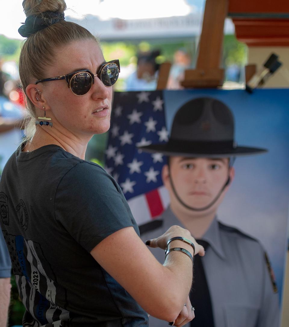 Stephanie Mack, widow of Pennsylvania State Trooper Martin Mack III, stands next to his portrait, Saturday, Aug. 13, 2022, during the second annual Unity Day in Bristol Borough.
