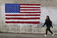 FILE - In this May 13, 2021, file photo, pedestrian walks in front of an American flag painted on a wall during the coronavirus outbreak in San Francisco. A number of states immediately embraced new guidelines from the CDC that say fully vaccinated people no longer need to wear masks indoors or out in most situations. But other states - and some businesses _ are taking a wait-and-see attitude. (AP Photo/Jeff Chiu, File)