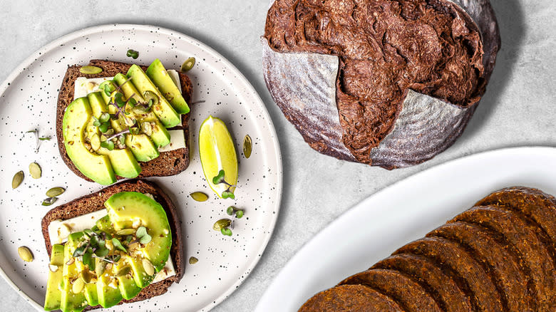 Avocado toast on pumpernickel slice next to loaf